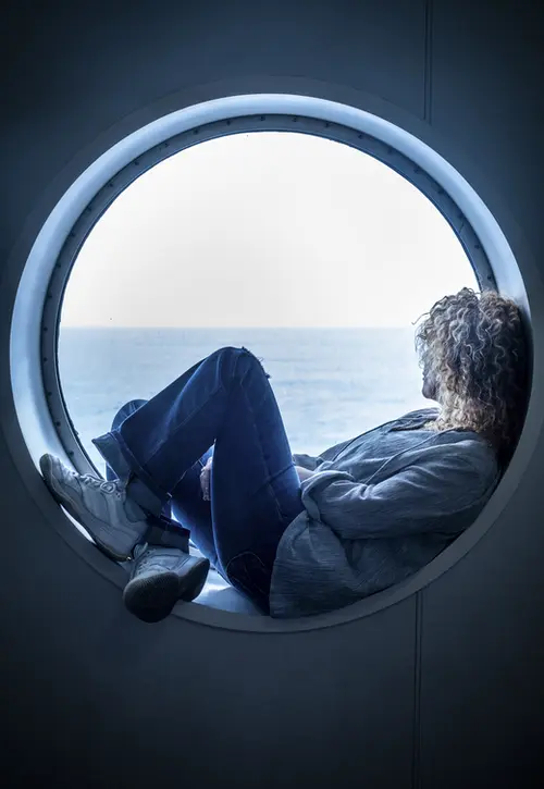 Traveler passenger woman sitting inside a porthole in the boat cruise enjoying the trip