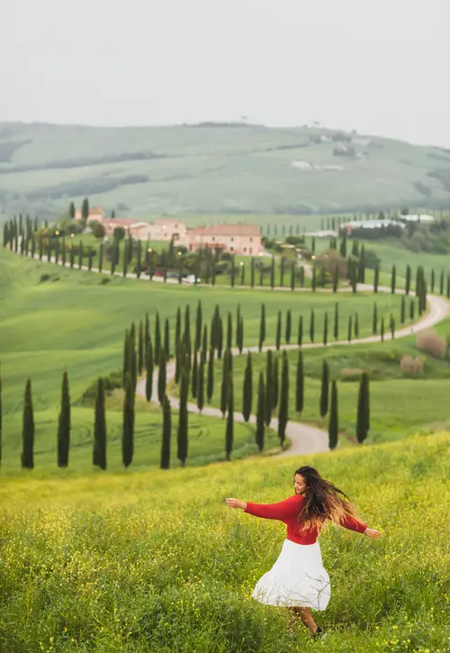 Woman in red sweater and white skirt on background on spring Tuscany landscape